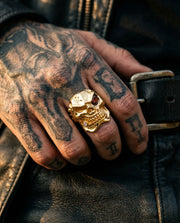 Heavy 14k gold plated skull ring featuring a red eye stone worn on a tattooed hand, representing bold men's biker jewelry style.