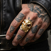 Heavy 14k gold plated skull ring featuring a red eye stone worn on a tattooed hand, representing bold men's biker jewelry style.