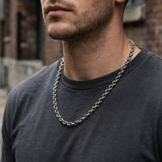Close-up of a man wearing a 5mm silver oval rolo chain necklace in an urban editorial style.