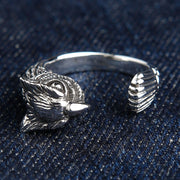 Anillo de búho en plata de ley 925, vista frontal que muestra los intrincados detalles del rostro y las plumas de la cola sobre fondo de mezclilla azul