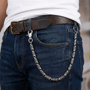 Close-up lifestyle shot of a heavy 925 silver rocker roller wallet chain attached to the belt loop of blue denim jeans, worn with a distressed brown leather belt and a white t-shirt.