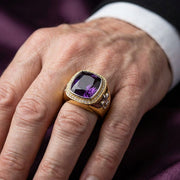 A mão de um modelo a usar o anel de bispo em ametista e ouro, maciço e luxuoso, para demonstrar o seu tamanho e estilo imponentes.