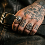 Sterling silver Bandana Biker Skull Ring featuring a brass mask and helmet design, worn on a tattooed hand resting on a black leather jacket for a rugged motorcycle jewelry look.