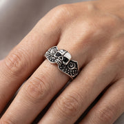 A close-up of a female hand wearing a wide 14mm black skull wedding ring under soft studio lighting.