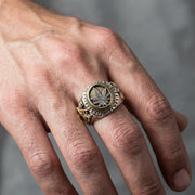 男性の手に着用された、詳細なカンナビスリーフデザインを特徴とするメンズスターリングシルバーと真鍮のバイカーリングのクローズアップ。