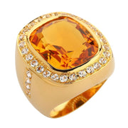 Top angled view of a faceted amber-gold citrine set in a thick yellow gold ring with a clear stone halo.