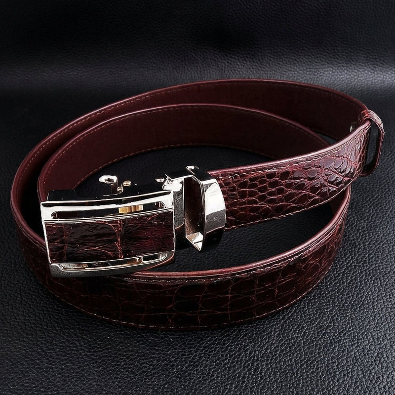 Cintura da uomo in vera pelle di coccodrillo marrone scuro con fibbia automatica argentata esposta su una superficie in pelle nera