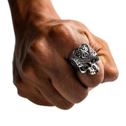 A man's hand wearing a big, ornate, and detailed Día de los Muertos ring with brilliant green gemstone eyes.