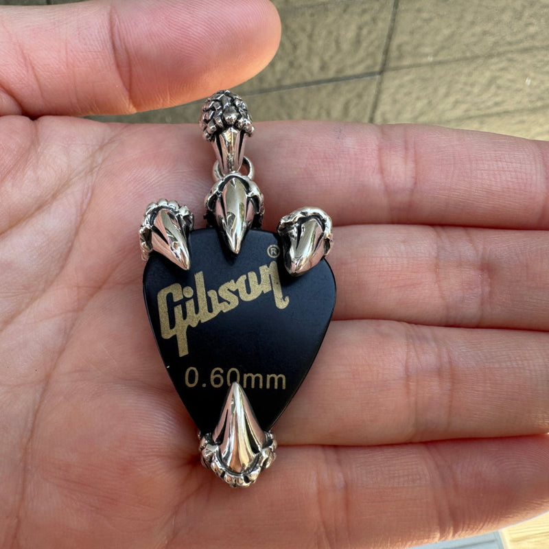 Pendentif en argent massif en forme de griffe de dragon tenant un médiator de guitare noir.