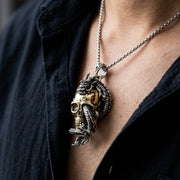 Close-up lifestyle photo of a person wearing a sterling silver chain necklace with a detailed dragon wrapped around a gold-tone skull pendant against a dark shirt.