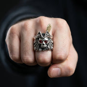 Man wearing feathered pirate skull ring with red CZ eyes making a fist, showing bold statement jewelry