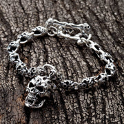A sterling silver flame skull link bracelet with a large skull clasp, shown on a dark wood background.