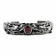 A heavy sterling silver cuff bracelet featuring two intricately carved dragons guarding a central oval red garnet stone.