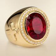 Angled view of a gold bishop ring with a 20-carat oval synthetic ruby, CZ diamond halo, and raised side cross.