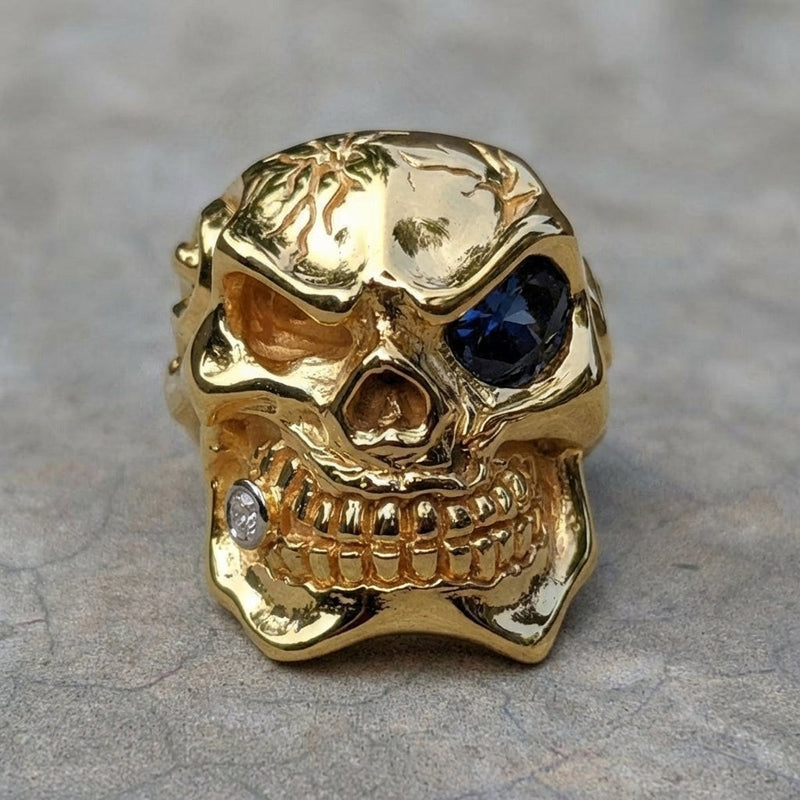 Vista frontale dell'anello a forma di teschio in argento sterling 925, realizzato a mano, con placcatura in oro 14K, caratterizzato da un occhio in pietra blu e un accento di diamante.