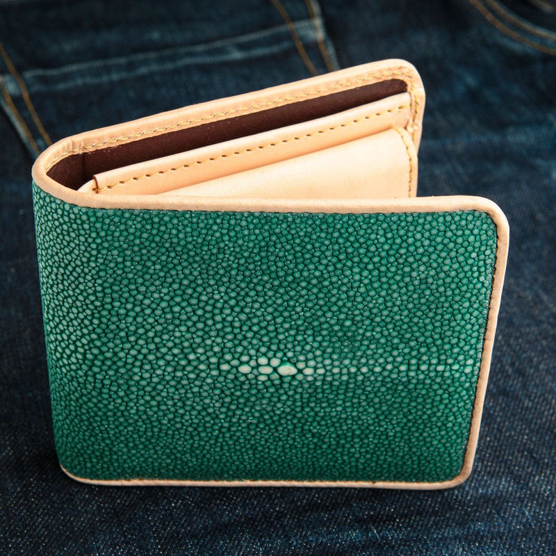 Portefeuille à deux volets pour homme en véritable cuir de galuchat vert émeraude avec garniture en cuir de vachette beige, sur fond de denim.