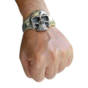 A man's wrist wearing a heavy, solid sterling silver biker skull cuff, showcasing its massive size.