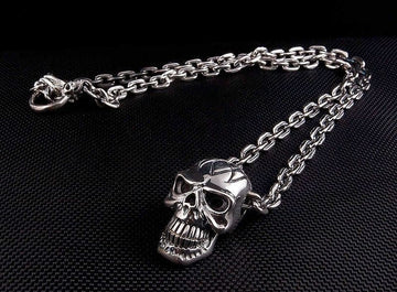 Un collar de calavera de plata esterlina pesado con una cadena de motociclista de 7 mm y un broche T-bar dispuesto en una superficie negra.