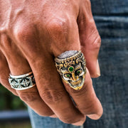 A heavy, two-tone Tibetan skull ring for men, handcrafted from sterling silver with gold highlights and green stones.