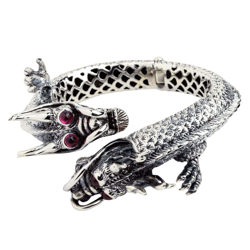Ein riesiges, schweres silbernes Armband in Form von zwei gegenüberstehenden Drachen mit roten Rubineaugen.
