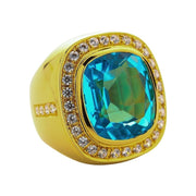 Angled view of a heavy warm gold ring featuring a large faceted ice blue topaz surrounded by a clear stone halo.