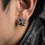 Close-up editorial shot of a rocker wearing 12mm iced out iron cross earrings under soft studio lighting.