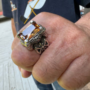 A man's hand wearing a massive sterling silver Imperial Topaz dragon claw ring with a golden-orange stone.