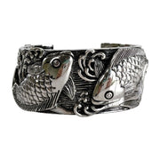 Vista frontal de un brazalete cuff macizo de plata esterlina de 38mm de ancho con dos peces koi tallados nadando entre olas en remolino.