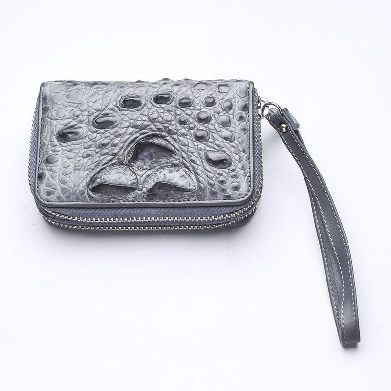 Portafoglio zip-around in vera pelle di coccodrillo grigio chiaro con squame a rilievo e cinturino da polso su sfondo bianco