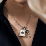 A close-up of a male model wearing a lock and key pendant featuring a detailed padlock and key charm under soft studio lighting.
