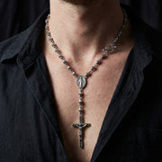 Een close-up redactionele fotografie van een man die een gotische Memento Mori schedel rozenkrans ketting draagt met een grote hanger en zware ketting.