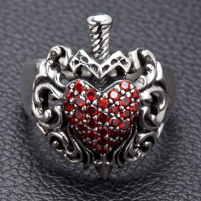 Un anello a forma di cuore con pugnale gothic per uomo, realizzato a mano in argento sterling e impreziosito da un pavé di pietre di granato rosso.