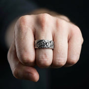 Herrars hammarsilverring med grov texturerad yta och korsat mönster, bärs på långfingret av en knuten näve mot en mörk bakgrund