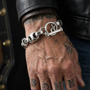 Close-up of a men's sterling silver Iron Cross bracelet with 15mm wide links, worn on a hand in a rocker pose under soft studio lighting.
