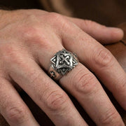 Close-up da mão de um homem a usar um anel de motociclista em prata esterlina robusta, apresentando um design de cruz celta elevada com detalhes oxidantes e pequenos acentos de cruz na banda texturizada.