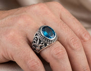 Man wearing a sterling silver biker ring featuring an intricate octopus tentacle design and a large oval blue topaz gemstone on his finger