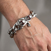 Men's heavy sterling silver biker bracelet featuring skulls with red garnet eyes worn on a wrist, showcasing gothic jewelry style.