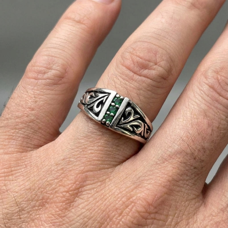 Bague en argent sterling pour homme avec émeraude tribale portée au doigt, présentant des sculptures tribales complexes et une rangée verticale d'émeraudes vertes.