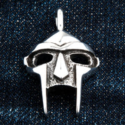 Front view of the sterling silver MF Doom mask pendant shown on a dark denim background.