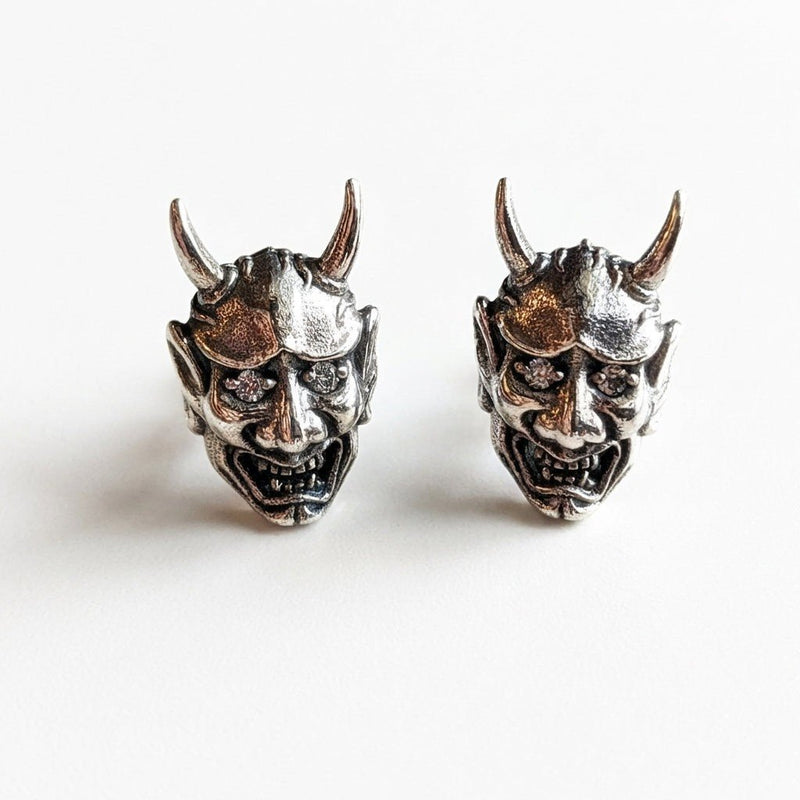 Front view of two Oni demon sterling silver earrings featuring curved horns, bared fangs, and diamond CZ stone eyes.