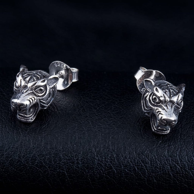 Pair of .925 silver tiger head studs facing forward on black leather, the 925 stamp visible on one butterfly back