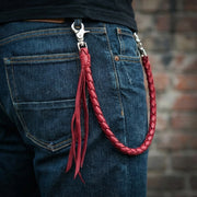 Rode bordeaux gevlochten leren portemonnee ketting met zilveren metalen clips bevestigd aan de achterzak van blauwe denim jeans, met decoratieve leren franjes.