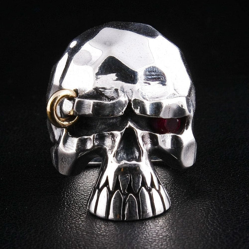 Cette bague de style punk à tête de mort aux yeux rouges est dotée d'une texture robuste et facettée et d'un piercing rebelle en or.