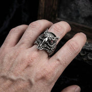 A close-up of a large sterling silver owl ring with red eyes worn on a male hand, captured in soft studio lighting with a gothic fashion aesthetic.