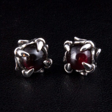 A pair of red garnet gothic claw stud earrings with silver dragon claws on a black background.