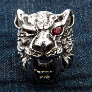 A massive sterling silver sabre tooth tiger ring with a single piercing red CZ eye, shown on a denim background.