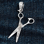 A close-up of the sterling silver scissors pendant on a dark denim background.