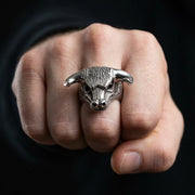 Anel em forma de cabeça de touro prateado com chifres texturizados e características faciais detalhadas exibido em um punho cerrado contra um fundo escuro