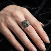 Oxidized silver owl band ring with intricate feather detailing worn on middle finger, showcasing detailed owl face design against black velvet background