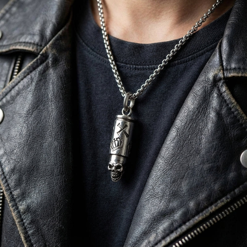 Collar con colgante de bala de calavera plateada usado por un hombre con chaqueta de cuero negra y camiseta oscura, que presenta un diseño cilíndrico grabado con detalle de calavera en la cadena.